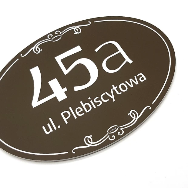 Owalna brązowa tabliczka na dom z przykładowym numerem i ulicą, pokazana pod kątem na białym tle