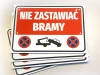 Tabliczka Nie zastawiać bramy - Wzór graficzny. Czerwone tło z białym napisem, symbolem holowania i znakami zakazu