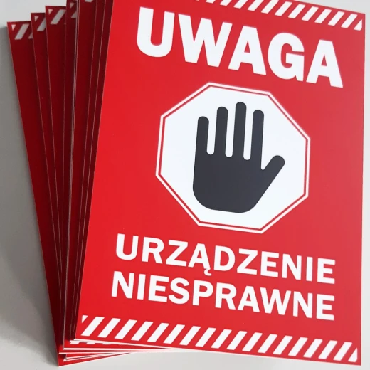 Stos czerwonych tabliczek ostrzegawczych BHP z napisem UWAGA URZĄDZENIE NIESPRAWNE i piktogramem dłoni