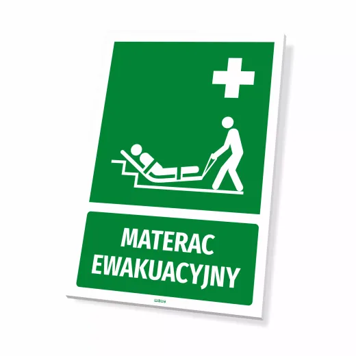 Zielona tabliczka BHP pierwsza pomoc z białym piktogramem i napisem Materac ewakuacyjny, ujęcie z ukosa