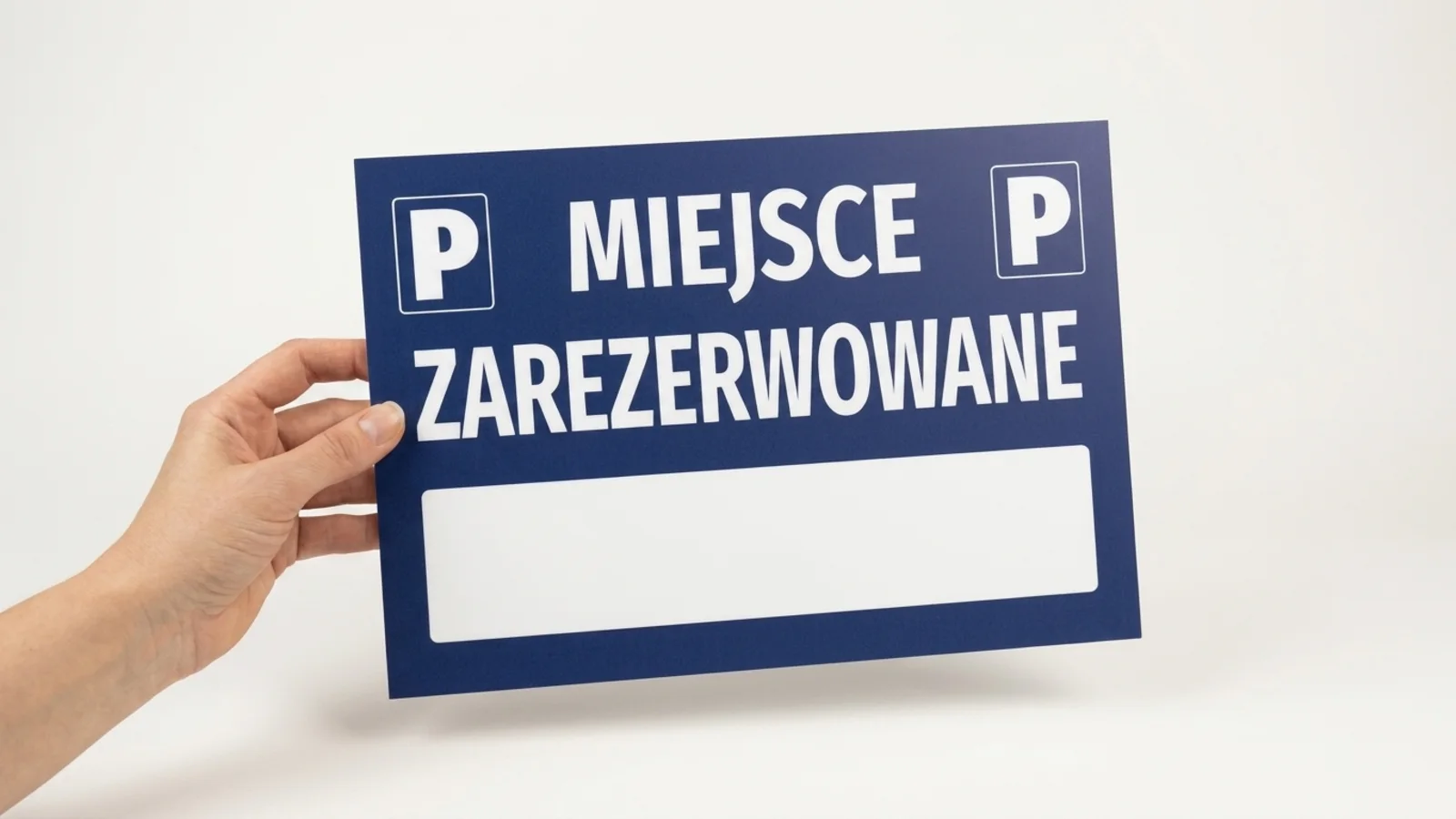 Dłoń trzyma granatową tabliczkę parkingową Miejsce zarezerwowane